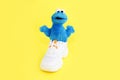 Soft fluffy children`s toy cookie monster in white shoes sneakers on a yellow background