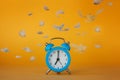 Soft fluffy flying feathers and blue alarm clock on yellow background Royalty Free Stock Photo