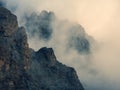 Dangerous gorge. Dramatic fog among giant rocky mountains. Ghostly atmospheric view to big cliff in cloudy sky. Low clouds and Royalty Free Stock Photo