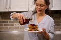 Soft focus on the hands of a beautiful female chef, charming pretty woman pouring maple syrup on a stack of homemade pancakes