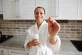 Soft focus on a medical pill in the hand of a blurred smiling woman in bathrobe standing at the kitchen