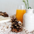 Soft focus of pine cone on white crocheted fabric with a glass of orange juice in the background