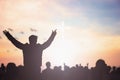 Praise and worship concept: Silhouette human raising hands to praying God on blurred cross with crown of throne sunset background Royalty Free Stock Photo