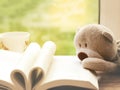 Soft focus of Teddy bear laying on open book like heart shape page, A shape of heart on book with teddy and cup of tea next to win Royalty Free Stock Photo