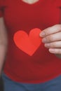 Soft focus. Young woman in a red T-shirt holds a red heart cut out of paper. Authentic photo. Close-up. Valentins Day, Mother`s