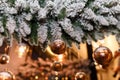 Soft focused shot of snowy fir-tree branches decorated with golden baubles and shiny garland lights bokeh on blurry background. Royalty Free Stock Photo