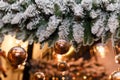 Soft focused shot of snowy fir-tree branches decorated with golden baubles and shiny garland lights bokeh on blurry background. Royalty Free Stock Photo