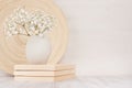 Soft home decor of beige bamboo dish and white small flowers in ceramic vase on white wood background. Interior.