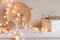 Soft home decor with burning lights on white wooden background.
