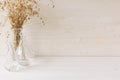 Soft home decor of glass vase with spikelets on white wood background.