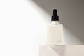 Soft light casts a subtle glow on a glass dropper bottle resting on a simple white pedestal, emphasizing its minimalist design Royalty Free Stock Photo
