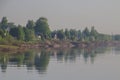 A soft misty sunny dawn on the river bank. Rustic small wooden houses along the coast, a summer original rural landscape Royalty Free Stock Photo