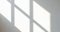 Soft sunlight casts geometric shadows of a window frame onto a light-colored wall. The shadows form Royalty Free Stock Photo