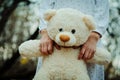 Soft toy bear on hands of girl on sleepwear outdoor.