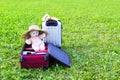 Soft toy bear in opened travel bag with clothes on green summer meadow