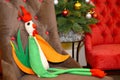 Soft toy rooster sits in a chair against the background of a New Year tree