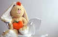 Soft toy-yellow hare with a heart in his hands on a wooden horse on a gray background space for text