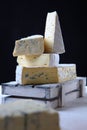 Soft white cheese with blue mold in a white wooden box on a black background. Vertical photo. Several pieces of cheese. Assorted