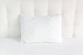 Soft white quilted pillow in bed on the background of white leather quilted headboard. Clean pillow, part of bed close-up, comfort