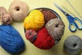 Soft woolen yarns, knitting needles and scissors on yellow background, flat lay