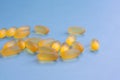 Soft yellow jelly chewable pills filled by fish oil as a source of Omega 3. Capsules are lying on blue background