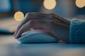 In a softly lit indoor environment during evening hours, a hand can be seen using a computer mouse that is positioned on Royalty Free Stock Photo