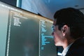 Software developer wearing glasses focuses on code displayed on a large monitor in a modern office, reviewing and debugging source Royalty Free Stock Photo