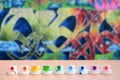 The soiled multicolored nozzles from the paint sprayer are lined up on a wooden table on a background of colored graffiti drawing