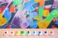 The soiled multicolored nozzles from the paint sprayer are lined up on a wooden table on a background of colored graffiti drawing