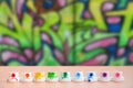 The soiled multicolored nozzles from the paint sprayer are lined up on a wooden table on a background of colored graffiti drawing