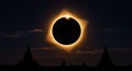 Solar eclipse over a dark landscape with silhouetted pagoda-like structures. The Royalty Free Stock Photo