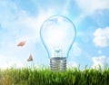 Solar energy concept. Glowing light bulb in grass and blue sky with clouds on background Royalty Free Stock Photo