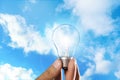 Solar energy concept. Man holding glowing light bulb against blue sky with clouds Royalty Free Stock Photo