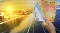 Solar Energy Economy, holding Brazilian money in front of the photovoltaic panel on a roof, sunset background