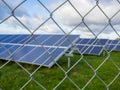 Solar panel or photovoltaic farm behind metal chainlink fence on green field with dramatic cloudy sky in North Germany Royalty Free Stock Photo