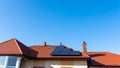 Solar panel on the red house roof in the background of blue sky.