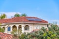 Solar panel on tile roof of house amidst lush foliage with blue sky background
