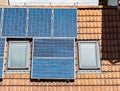 Solar panels on the tiled red roof of suburban house with roof windows Royalty Free Stock Photo