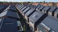 Solar panels are installed on the tiled roofs of a row of modern houses in a suburb with green streets under a blue sky Royalty Free Stock Photo