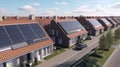 Solar panels are installed on the tiled roofs of a row of modern houses in a suburb with green streets under a blue sky Royalty Free Stock Photo