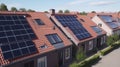 Solar panels are installed on the tiled roofs of a row of modern houses in a suburb with green streets under a blue sky Royalty Free Stock Photo