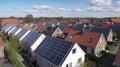 Solar panels are installed on the tiled roofs of a row of modern houses in a suburb with green streets under a blue sky Royalty Free Stock Photo