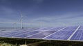 Solar panels with wind turbines against blue sky background. Royalty Free Stock Photo