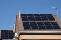 Solar photovoltaic panels on neighbourhood house roof against blue sky Royalty Free Stock Photo