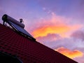 Solar water heater boiler on rooftop, sunrise, cold morning, orange clouds on blue sky