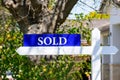 Sold real estate sign on wooden post. Blurred green landscaping background