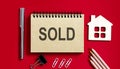 SOLD text written on a notebook with pencils and office tools and model wooden house Royalty Free Stock Photo