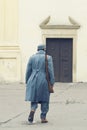 Soldier of Austro-Hungarian Army with a rifle on his shoulder walking into a closed roman Catholic church s door. Winter grey unif