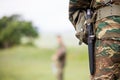 Soldier` body with camo clothing and knife in his belt. Close up behind view, blurred soldier and nature background, copyspace. Royalty Free Stock Photo