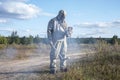 A soldier in a chemical protection suit checks the radioactive territory with a dosimeter against the background of wild vegetatio